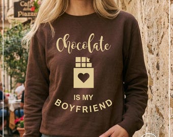 May include: A dark brown long-sleeve sweatshirt featuring the light tan text "Chocolate IS MY BOYFRIEND" and a graphic of a chocolate bar with a heart shape in the center. The design is centered on the chest of the garment.