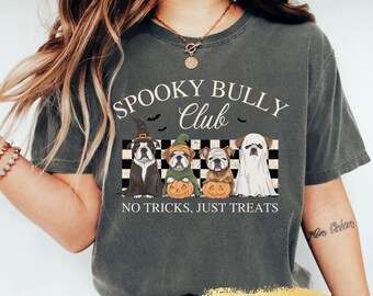 May include: Dark grey t-shirt with the text "Spooky Bully Club" and the phrase "No Tricks, Just Treats." The shirt features a graphic of four bulldogs dressed in Halloween costumes, including a witch, a ghost, and holding pumpkins.