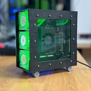 Peut inclure: Un boîtier d'ordinateur noir avec un panneau latéral transparent, révélant les composants internes. Le boîtier est doté de trois ventilateurs à LED verts sur le côté et repose sur quatre roues.