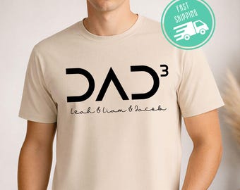 May include: Sand-colored t-shirt with the word "DAD³" in black, with the names "Leah & Liam & Jacob" below in a script font. The shirt has a crew neck and short sleeves. A "Fast Shipping" graphic is visible.