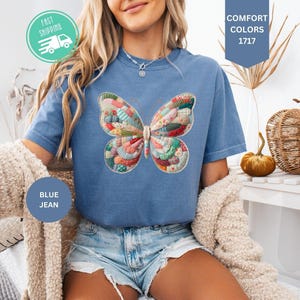 以下が含まれることがあります： カラフルな蝶のデザインが施された、ブルーデニムの半袖Tシャツ。 蝶は、赤、青、緑、黄色のパッチワーク模様です。 シャツには「Comfort Colors 1717」の文字も入っています。