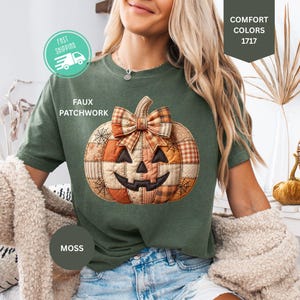 May include: A moss green short-sleeve t-shirt featuring a central graphic of a jack-o'-lantern pumpkin with a faux patchwork design in shades of orange and brown, topped with a plaid bow. The shirt includes text reading FAUX PATCHWORK.