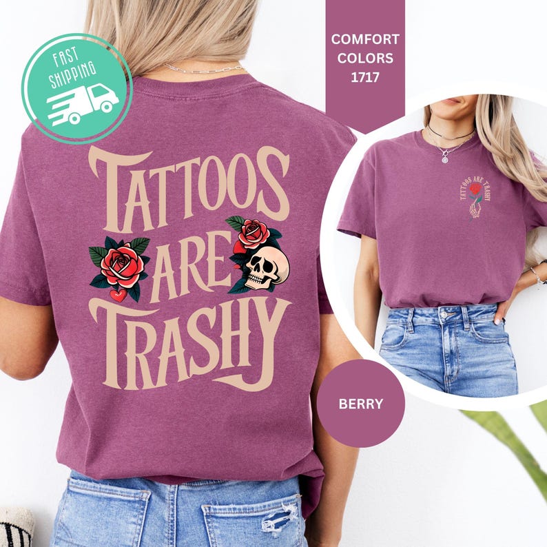 May include: A berry-colored t-shirt featuring the text TATTOOS ARE TRASHY in large beige letters on the back, accompanied by red rose and skull graphics. The front chest area displays a smaller version of the same text and a rose graphic.