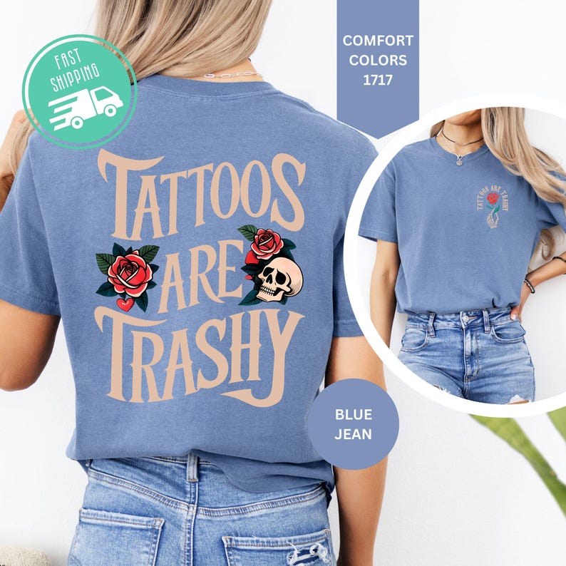 May include: A blue jean colored t-shirt featuring the text "TATTOOS ARE TRASHY" in a large, curved font on the back, accompanied by illustrations of red roses and a skull. The front chest area displays a smaller version of the same graphic.