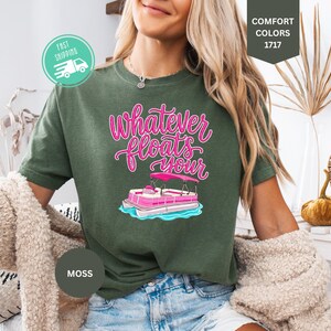Op de afbeelding: Mosgroen T-shirt met de tekst "Whatever Floats Your" in roze script, met een roze en witte pontonbootafbeelding. Het shirt is van het merk Comfort Colors.