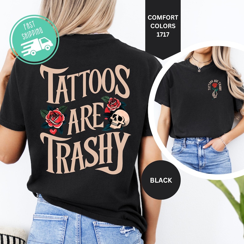 May include: A black t-shirt featuring the text TATTOOS ARE TRASHY in large beige letters on the back, accompanied by red rose and skull graphics. The front chest area displays a smaller graphic of a hand holding a rose with the same text.