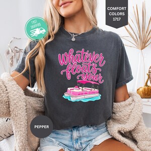 Op de afbeelding: Donkergrijs T-shirt met de tekst "Whatever Floats Your" in roze script, met een roze en witte pontonboot afbeelding. Het shirt is een Comfort Colors 1717 stijl.