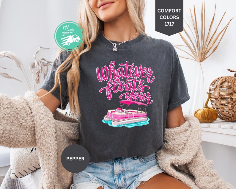 Op de afbeelding: Donkergrijs T-shirt met de tekst "Whatever Floats Your" in roze script, met een roze en witte pontonboot afbeelding. Het shirt is een Comfort Colors 1717 stijl.