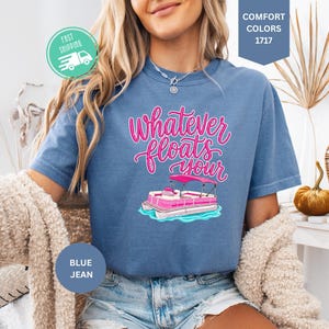 Op de afbeelding: Blauw spijkerbroekkleurig T-shirt met de tekst "Whatever Floats Your" in roze script, met een cartoon pontonboot. Het shirt heeft een ronde hals en korte mouwen. De afbeelding bevat ook een snel verzendpictogram.