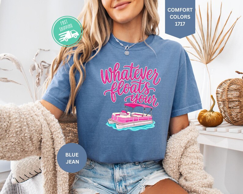Op de afbeelding: Blauw spijkerbroekkleurig T-shirt met de tekst "Whatever Floats Your" in roze script, met een cartoon pontonboot. Het shirt heeft een ronde hals en korte mouwen. De afbeelding bevat ook een snel verzendpictogram.