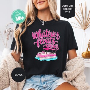 Op de afbeelding: Zwart T-shirt met de roze tekst "Whatever Floats Your" en een roze en witte pontonbootafbeelding. Het shirt is in Comfort Colors 1717-stijl.