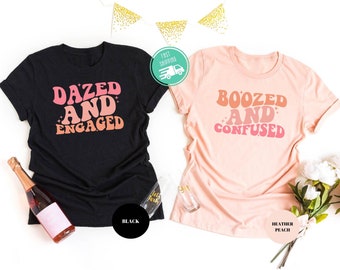 May include: Two t-shirts with a retro font design. The black t-shirt says "Dazed and Engaged" and the peach t-shirt says "Boozed and Confused".