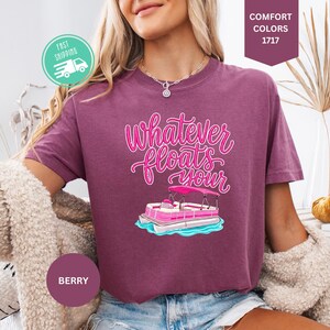 Op de afbeelding: Bessenkleurig T-shirt met de tekst "Whatever Floats Your" in roze script, met een cartoon pontonboot. Het shirt heeft korte mouwen en is gemaakt van een zacht materiaal. Het shirt wordt gecombineerd met een blauwe spijkerbroek.