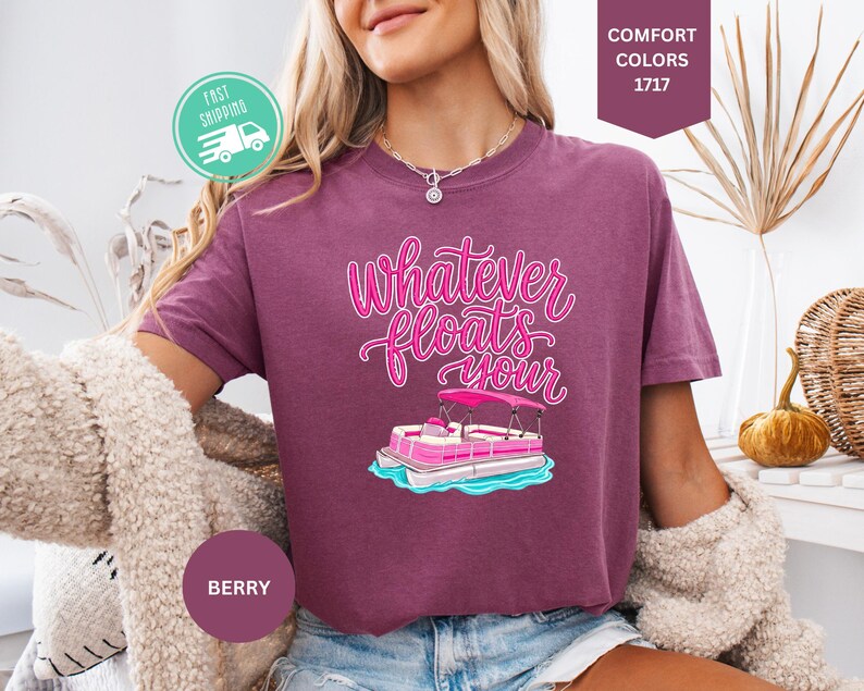 Op de afbeelding: Bessenkleurig T-shirt met de tekst "Whatever Floats Your" in roze script, met een cartoon pontonboot. Het shirt heeft korte mouwen en is gemaakt van een zacht materiaal. Het shirt wordt gecombineerd met een blauwe spijkerbroek.