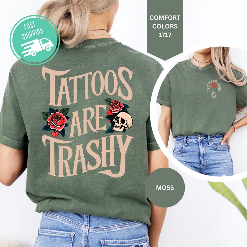 May include: A moss green t-shirt featuring the text "TATTOOS ARE TRASHY" in large beige letters on the back, accompanied by red rose and skull illustrations. A smaller version of the same graphic is printed on the front left chest area.