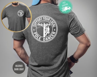 May include: A heather dark gray t-shirt with a white graphic on the back. The graphic is a circle with the text "Support Your Local Pole Dancer" and a silhouette of a person climbing a utility pole.