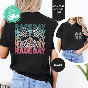 May include: A black t-shirt featuring a large graphic on the back with the text RACEDAY repeated in distressed teal, yellow, pink, and red colors behind a large black and white checkered bow. A smaller version of the bow is on the front left chest.