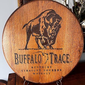 May include: Circular wooden sign featuring the "Buffalo Trace" logo and a bison illustration. The sign is made from a whiskey barrel section and includes the text "Kentucky Straight Bourbon Whiskey".