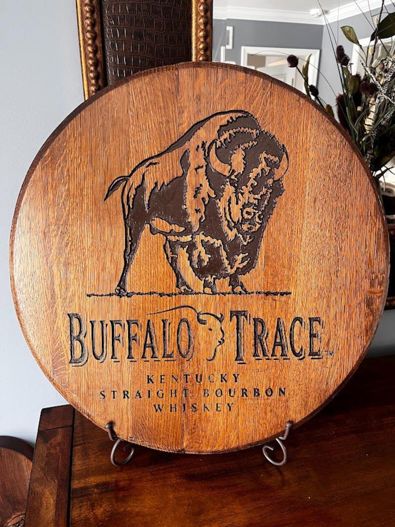 May include: Circular wooden sign featuring the "Buffalo Trace" logo and a bison illustration. The sign is made from a whiskey barrel section and includes the text "Kentucky Straight Bourbon Whiskey".