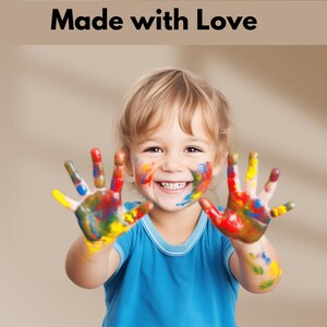 Peut inclure: Un jeune enfant avec de la peinture color&eacute;e sur les mains et le visage sourit &agrave; la cam&eacute;ra. L'enfant porte une chemise bleue.