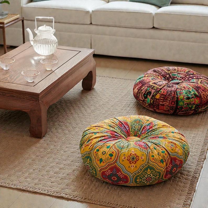 May include: Two round floor cushions with colorful, patterned fabric. One cushion is primarily yellow with red, green, and blue accents. The other is predominantly red with similar colors. They sit on a neutral-colored rug.
