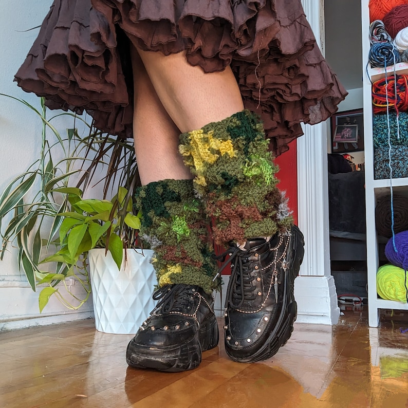 May include: A pair of black platform shoes with chunky soles and silver buckles. The shoes are worn with green and brown crocheted leg warmers.