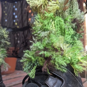 May include: Green, brown, and yellow fuzzy yarn boot cuffs. The cuffs are made of a thick, fluffy yarn and are perfect for adding a touch of whimsy to any outfit.