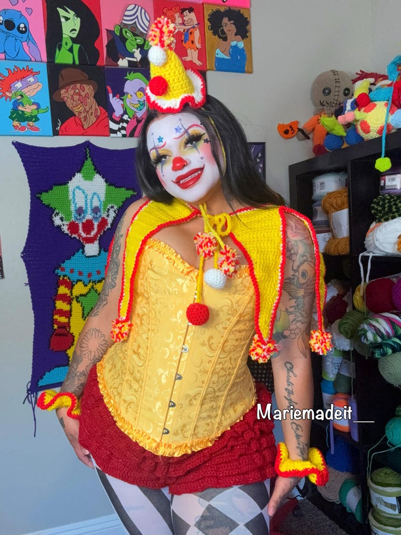 May include: A yellow and red crochet clown costume. The costume includes a yellow corset, a red ruffled skirt, a yellow cape with red trim, and a matching hat. The image also includes yellow and red wrist cuffs. The text "Mariemadeit_" is visible.