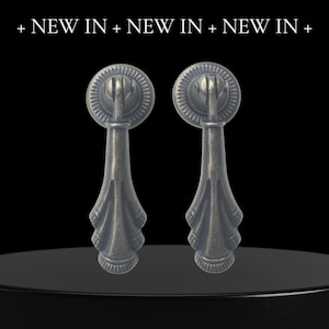 May include: Two antique bronze-effect drawer pulls with a decorative design. Each pull has a circular top with a handle and a teardrop-shaped base. The text "+ NEW IN + NEW IN + NEW IN +" is at the top.