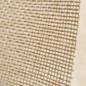 May include: Close-up of a beige burlap fabric with a woven texture. The fabric has a tight weave and a slightly rough surface.