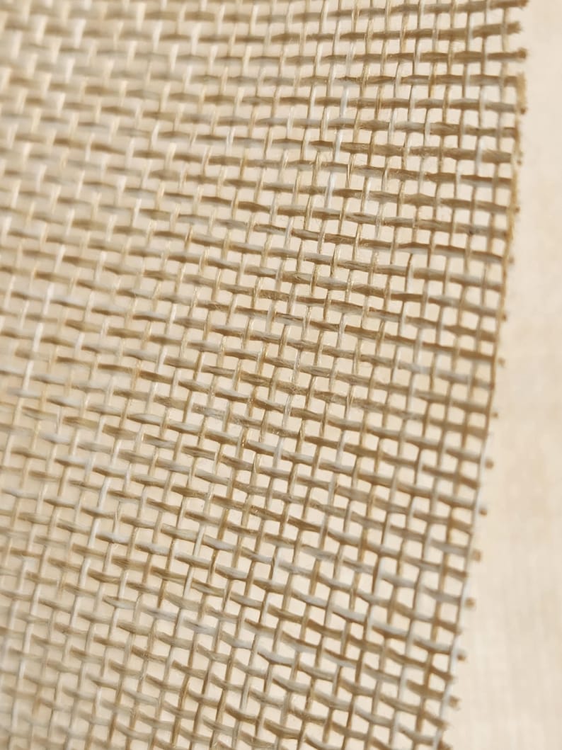 May include: Close-up of a beige burlap fabric with a woven texture. The fabric has a tight weave and a slightly rough surface.