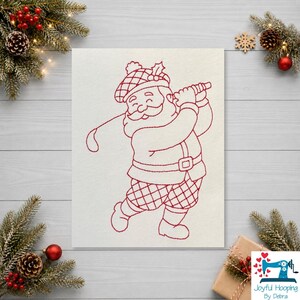 Pode incluir: Um design de bordado à máquina vermelho sobre fundo branco apresentando o Papai Noel usando uma boina escocesa e calças xadrez enquanto balança um taco de golfe. O design inclui o texto Joyful Hooping By Debra no canto inferior.