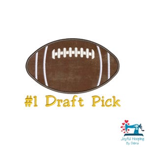 Puede incluir: Un balón de fútbol americano marrón con rayas y cordones blancos. El texto "#1 Draft Pick" está en escritura dorada debajo del balón. La imagen está sobre un fondo blanco.