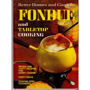 May include: A vintage cookbook cover titled "FONDUE and TABLETOP COOKING" by Better Homes and Gardens. The cover features a yellow fondue pot with a piece of food on a fork, lit candles, and text about recipes and party ideas.