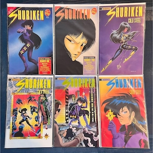 May include: A collection of six comic books titled "Shuriken: Cold Steel." Each cover features a stylized illustration of a female character in action poses, with vibrant colors and dynamic compositions. The comic books are numbered and include text.