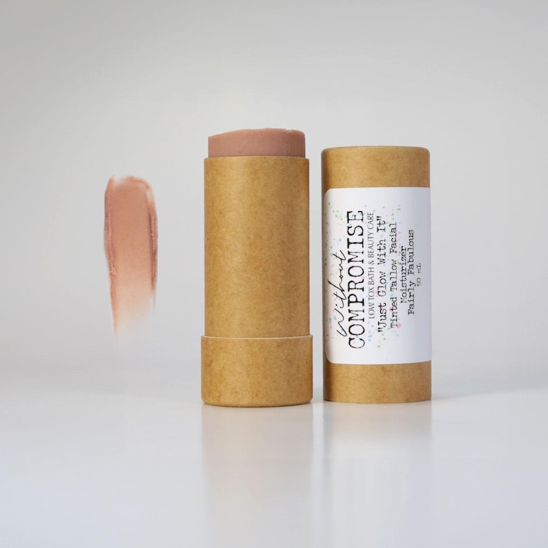 May include: A brown cardboard tube with a white label that reads "Without Compromise Low Tox Bath & Beauty Care "Just Glow With It" Tinted Tallow Facial Moisturizer Fairly Fabulous". The tube contains a light brown tinted balm.