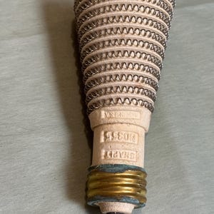 以下が含まれることがあります： アンティークのSnapit No. 355電気ヒーターエレメント。エレメントは、銀色のコイル状ワイヤーで包まれたベージュ色のセラミックボディです。ベースは真鍮製で、小さな金属製の先端が付いています。「MADE IN USA」の文字が見えます。