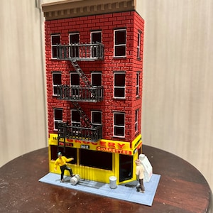 Puede incluir: Un edificio de ladrillo rojo con una fachada amarilla que dice "Grocery, Fruits, Ice, Cigarettes". Hay dos figuras de pie frente al edificio. El edificio tiene una escalera de incendios y un techo marrón.