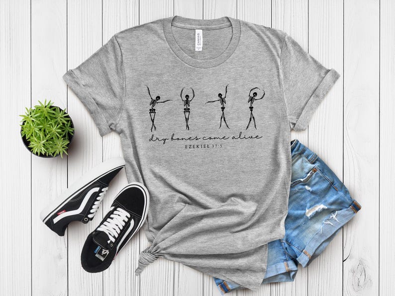 a gray t-shirt with a graphic design, a pair of black and white sneakers, and a pair of blue denim shorts, all laid out on a white wooden surface.