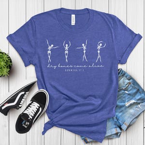 a blue t-shirt with a graphic design, a pair of black and white sneakers, and a pair of blue denim shorts, all laid out on a white wooden surface.