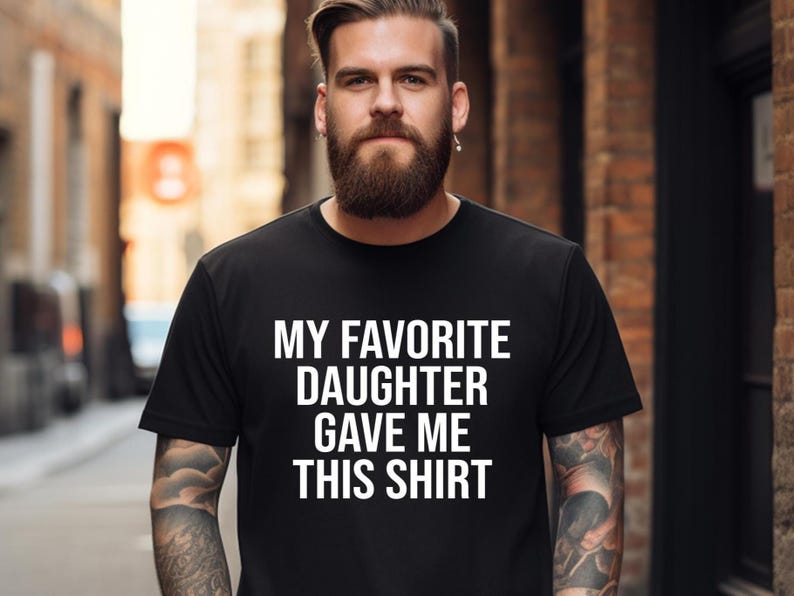 May include: A person wearing a black t-shirt with the text 'My Favorite Daughter Gave Me This Shirt' printed in white.