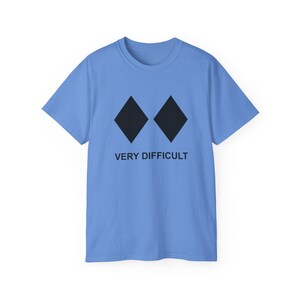 May include: A pale blue t-shirt featuring two black diamond symbols and the text "VERY DIFFICULT" underneath. The tee shirt has a crew neck and is likely made of cotton.