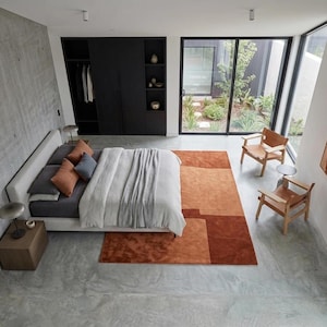 Designer bedroom styling, terracotta modern wool area rug at bed foot, minimalist geometric layout