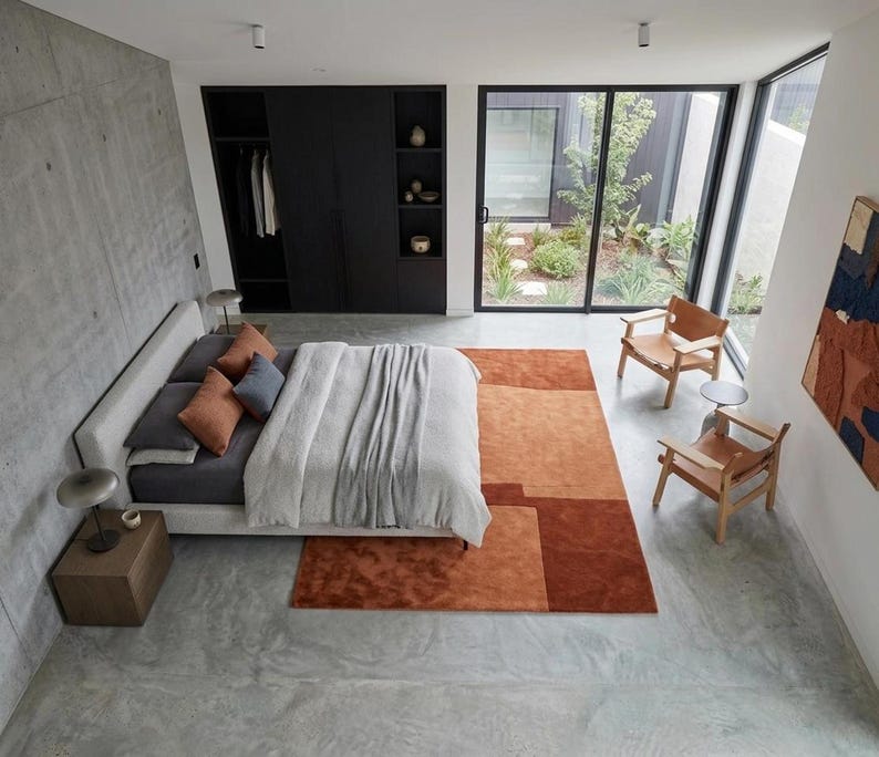 Designer bedroom styling, terracotta modern wool area rug at bed foot, minimalist geometric layout