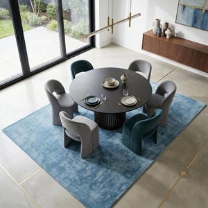 May include: A modern dining room set featuring a round dark wood table with six curved-back chairs in gray and teal. The table is set with plates and small bowls. The chairs sit on a large, light blue rug. A modern light fixture hangs above the table.