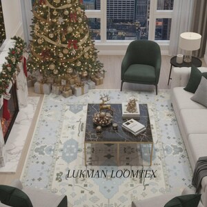 May include: A patterned area rug in cream and light blue tones, with a geometric design, is in a living room setting. A decorated Christmas tree is in the background. The rug features the text "LUKMAN LOOMTEX".