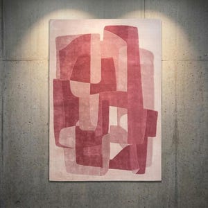 May include: A rectangular rug with an abstract design in shades of red and pink. The rug features overlapping geometric shapes, creating a layered effect. The rug is displayed against a grey concrete wall, illuminated by a spotlight.