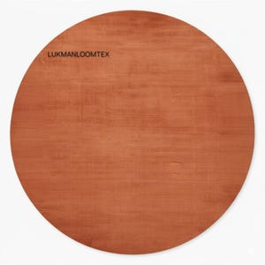 May include: A circular, terracotta-coloured rug with the text "LUKMANLOOMTEX" in the upper left corner. The rug has a smooth texture and is set against a white background. This rug is suitable for home decor.