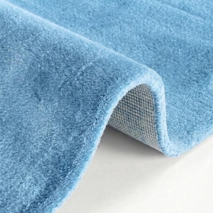 May include: A close-up of a rolled-up, light blue rug. The rug has a soft, plush texture and a visible backing. The color is a solid, muted blue, and the rug appears to be made of a thick, durable material. The rug is likely for home decor.