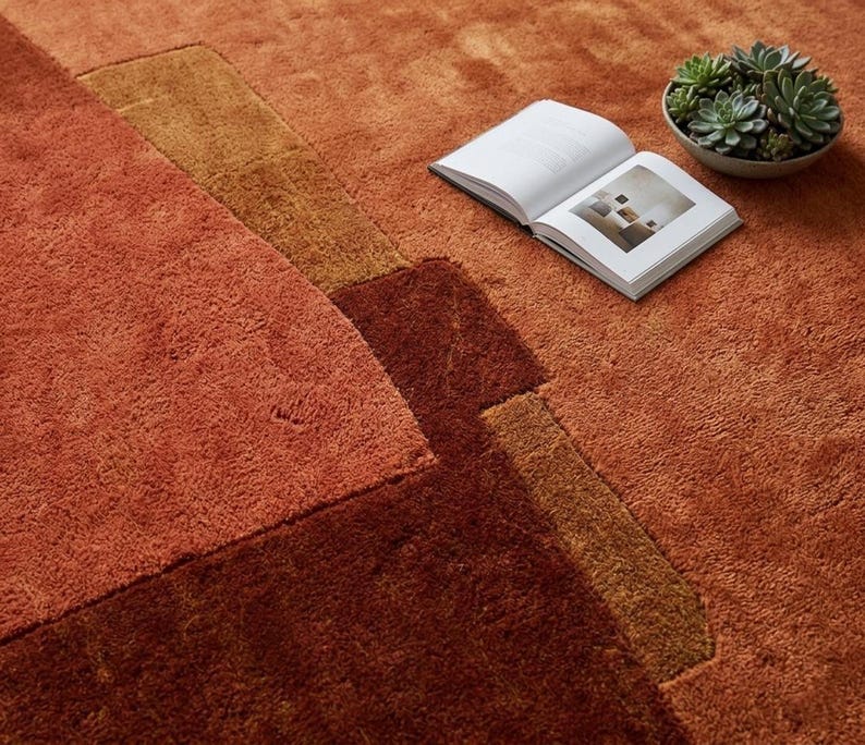 Close-up hand tufted wool rug, rich terracotta and rust blocks, dense plush pile and carving detail